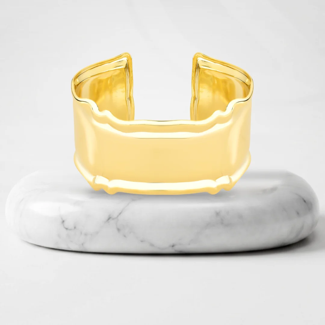 Wide cuff bracelet with Quebec gold plating on a marble pedestal
